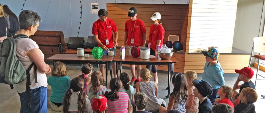 Three volunteers do a demonstration for a large group of children on a field trip.