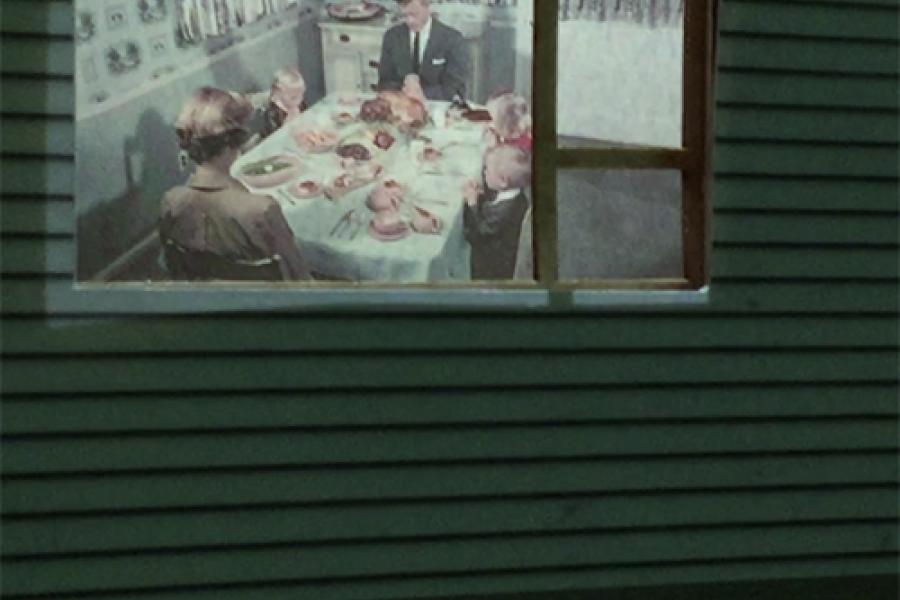 Images of traditional western family dinner projected onto the window of a suburban home