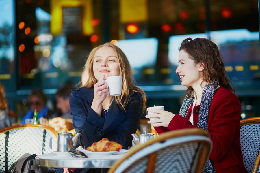 Two women sitting at outdoor cafe with coffees and croissants.