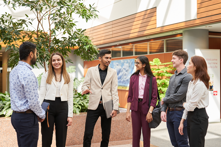 A group of Asper students in business clothing standing and talking in a lobby.