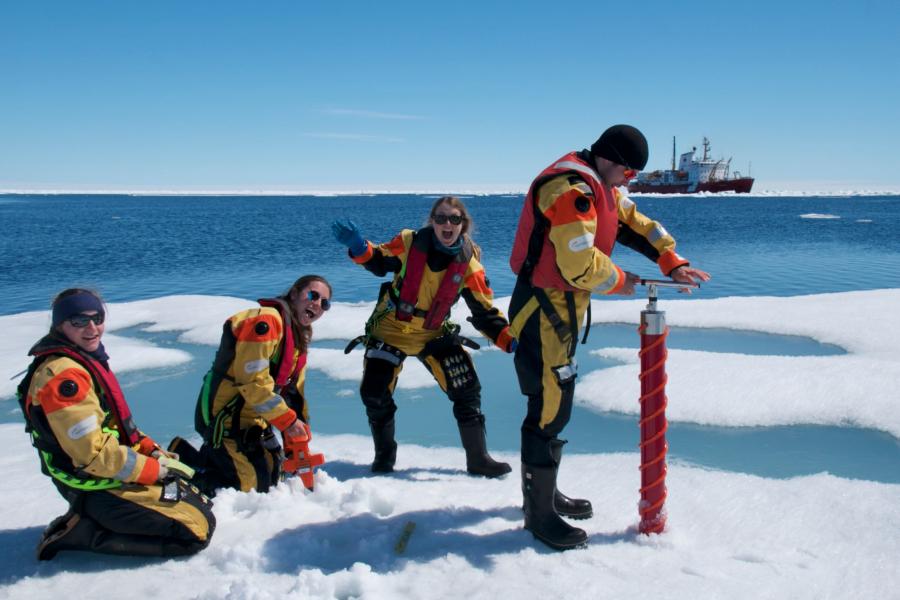 Researchers smiling and enjoying their time on the sea ice as one of them cores the ice