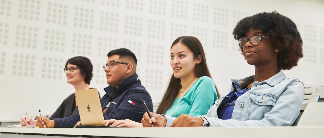 Four attentive students seated together side by side in a classroom. 