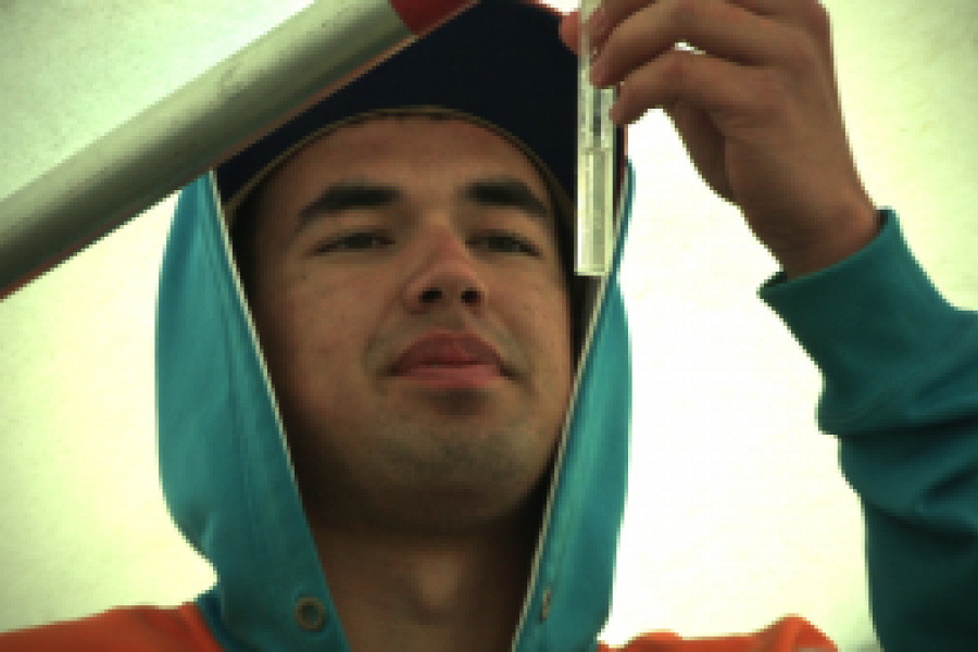 A student in a blue hoodie examining a vial of liquid.