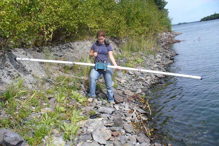 student using a pole to measure lake levels at shoal lake.