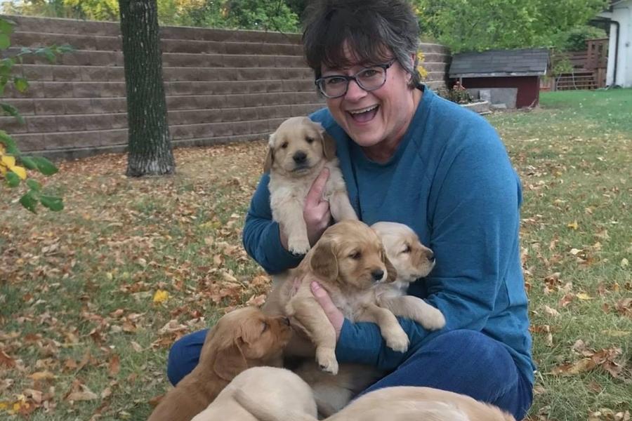 Karen wiens in a blue sweater holding a swarm of puppies.