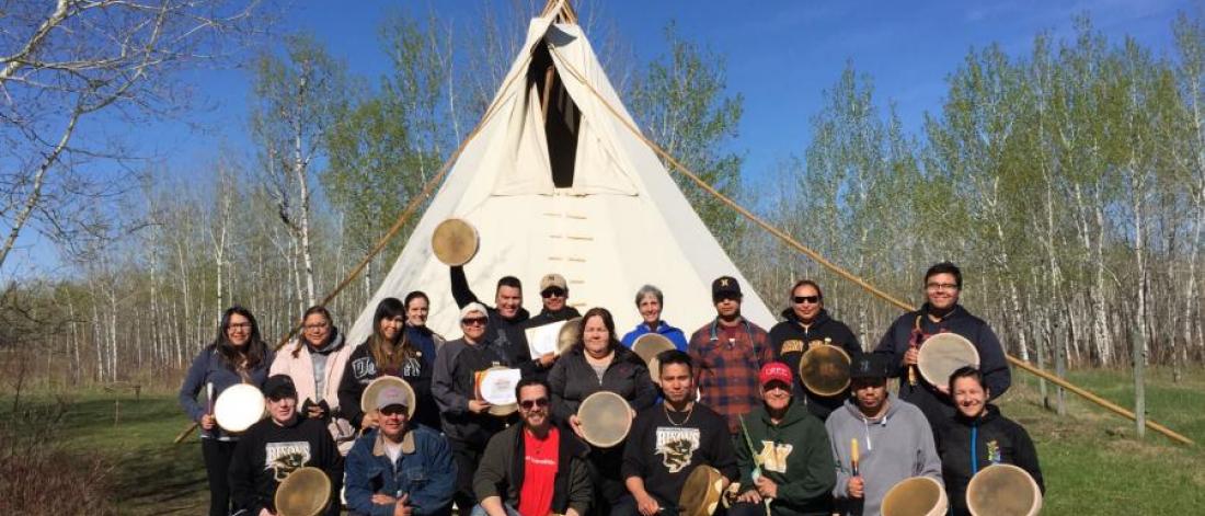 a group of Indigenous community members posing for a photo in front Teepee