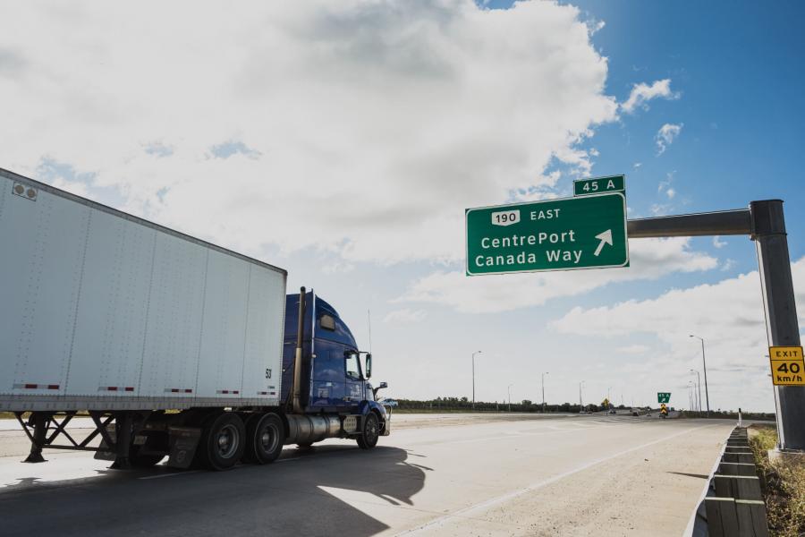 A transport truck drives down a highway passing a sign that reads 'CentrePort Canada Way'.