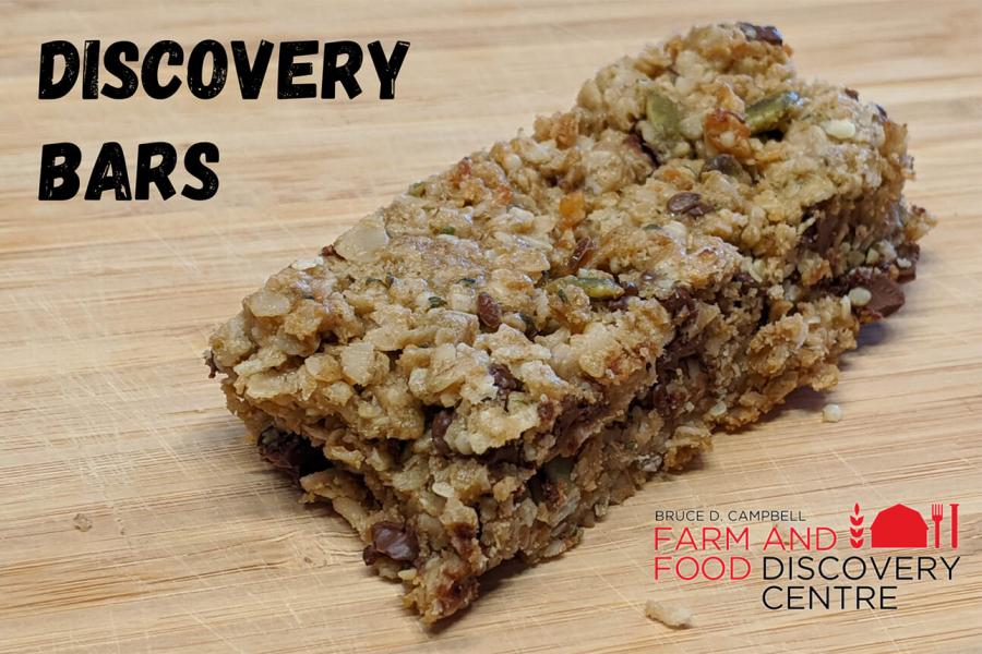 A rustic homemade granola bar sitting on a wooden cutting board with the title "Discovery Bars". 