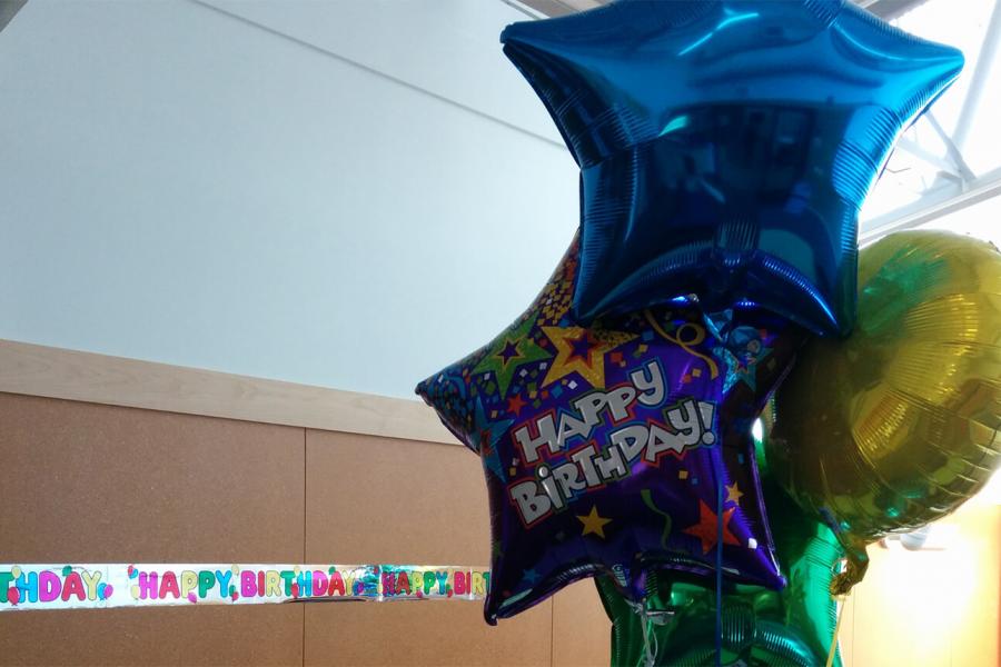 Three blue and green metallic balloons, one with the words "Happy Birthday" float in FFDC's classroom in front of a "Happy Birthday" banner.