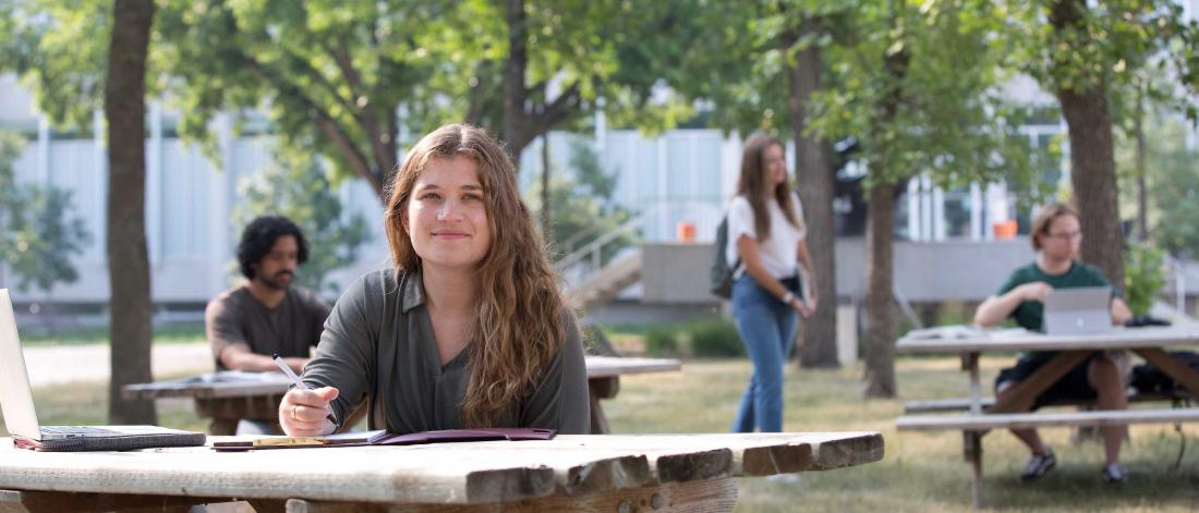 Smiling student sitting at picnic table on campus.