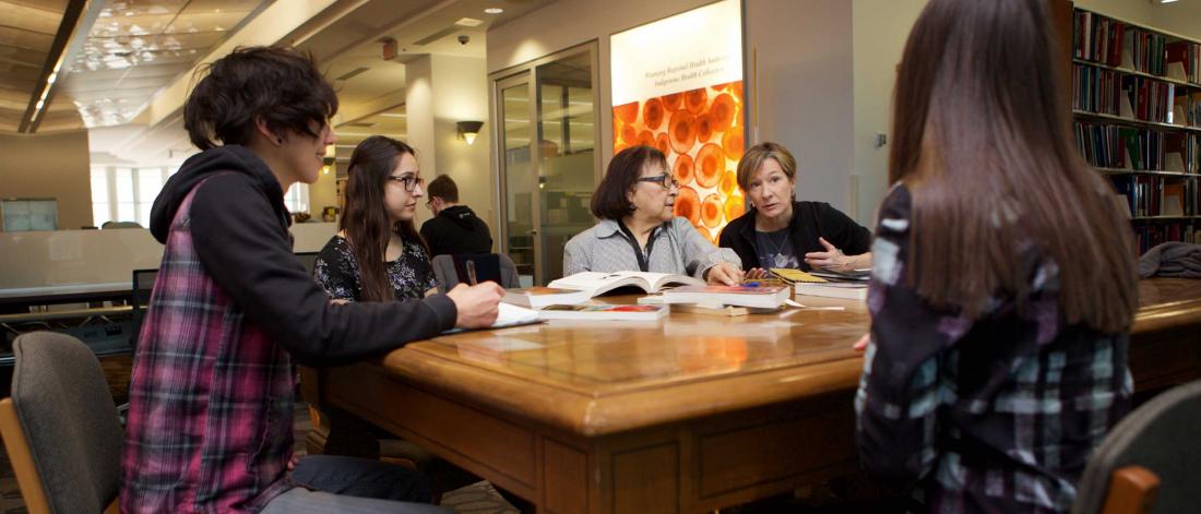 Students and Elder-In-Residence Margaret Lavallee study together in a library.