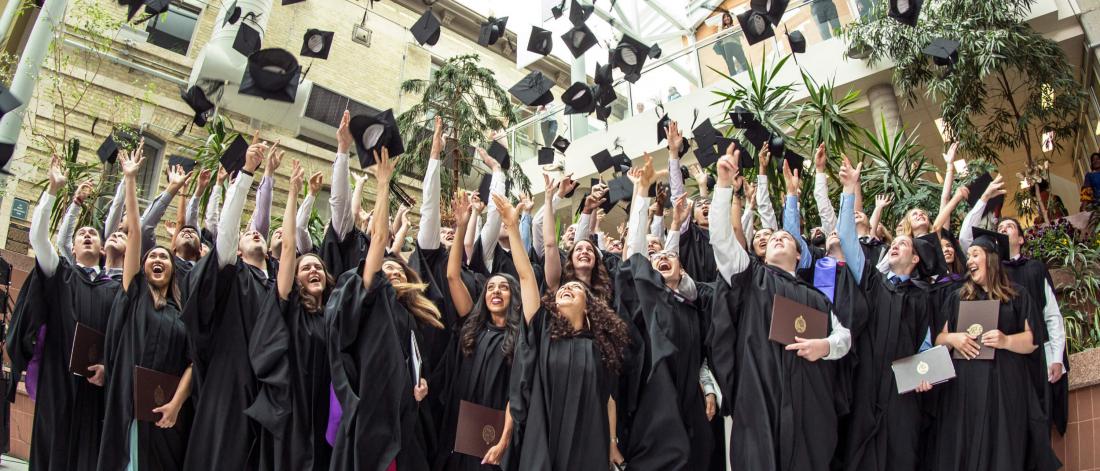 University of Manitoba students celebrate their graduation by tossing their mortarboard caps in the air together.