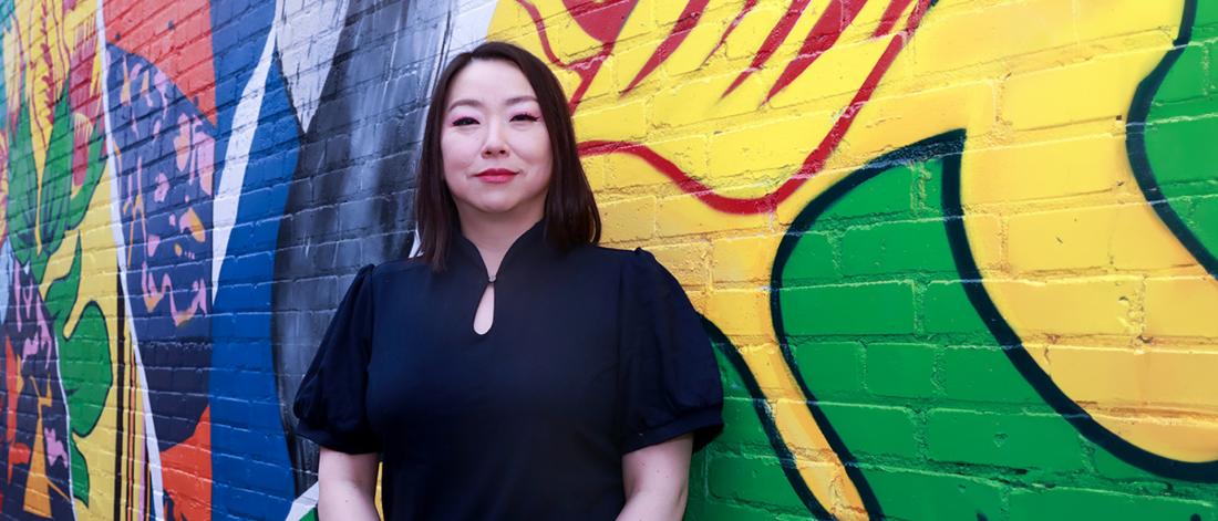 Hee-jung Serenity Joo, outgoing director of UM Institute for Humanities, and English, theatre, film, and media professor, in front of a mural at 116 Sherbrook by Real Fresh Canvas Co (Annaliza Toledo & Trevor Peters).
