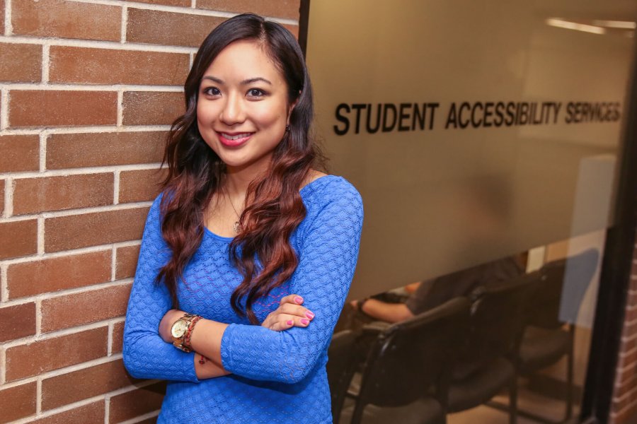 A smiling woman stands outside of the Student Accessibility Services office.