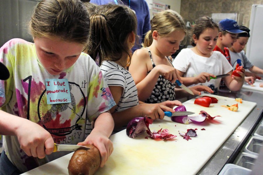 Kids preparing and cutting vegetables in a kitchen.