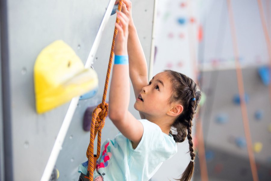 A young climber looks up to find a handhold while scaling a climbing wall.