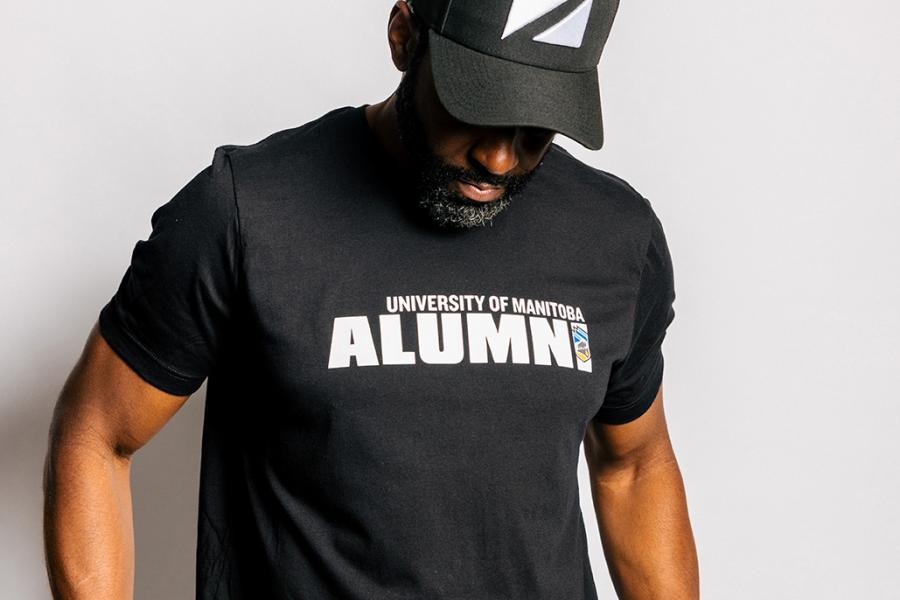A male model wearing a black UM alumni tshirt and hat.