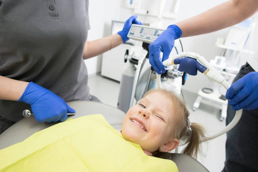 A child laying back in a dentist chair, smiling.