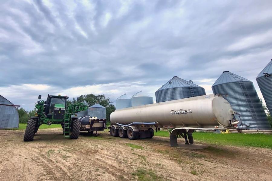 A tractor moves a cylinder trailer past some silos