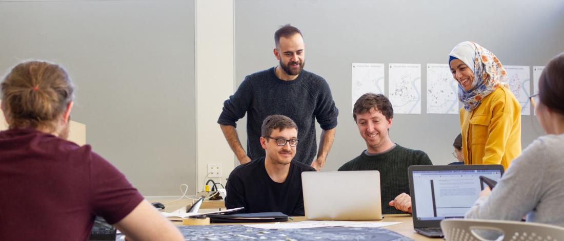 Several city planning students sit at a table working on laptops.