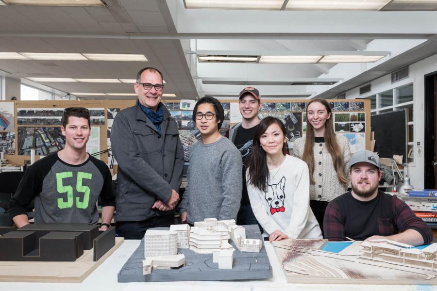Students gather around a table of projects with their instructor in the architecture studio.