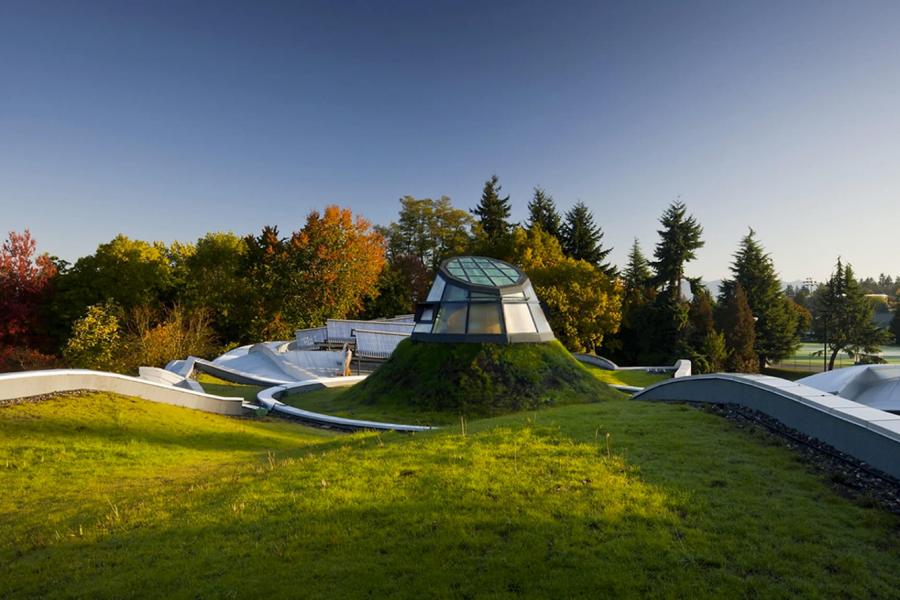 A beautiful landscape with grassy hills, trees and a glass dome structure emerging from the ground.