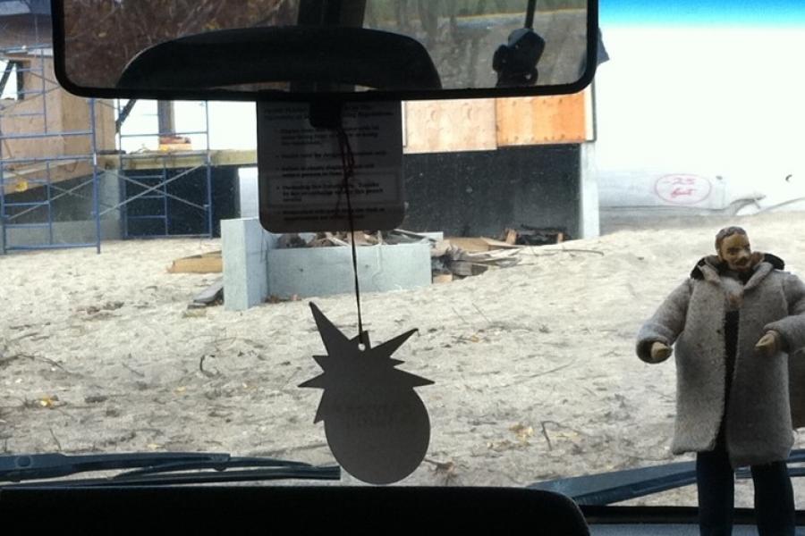 Car dash board looking at construction site with pineapple shaped air freshener and figure of man with a oversize coat