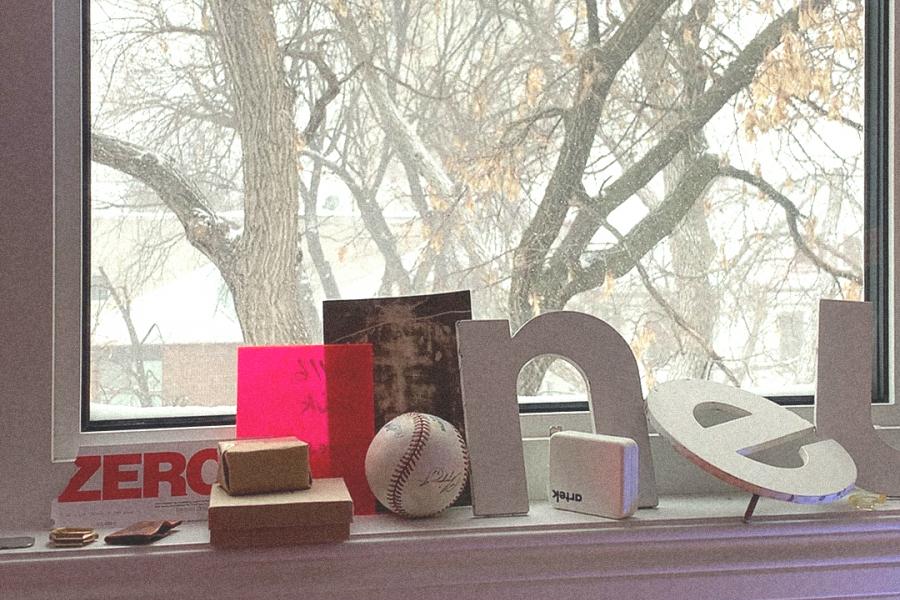 window looking out to snowy tree with a sill covered with items such as baseball, cutout letters and printed pictures