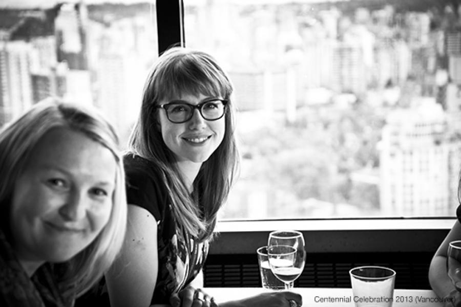Two people sit at a table by a large window overlooking a blurred city skyline, smiling and enjoying the soft, illuminated atmosphere.