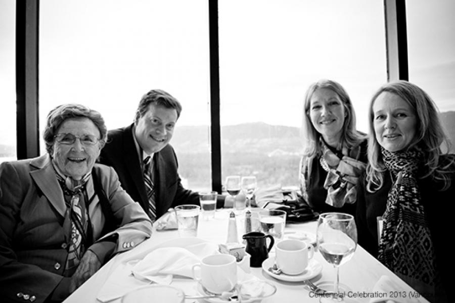 Four people sit at a dining table by a large window with a rolling hills view, smiling and enjoying a convivial atmosphere.