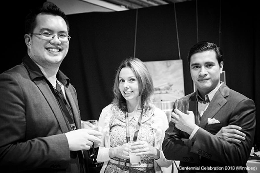 Three individuals stand together indoors, each holding a drink, suggesting a formal or celebratory event backdrop.