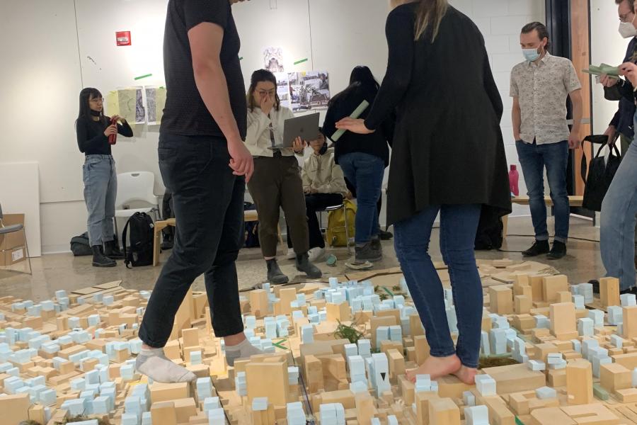 People examining a large cityscape model laid out on the floor in a room with high ceilings and ductwork.