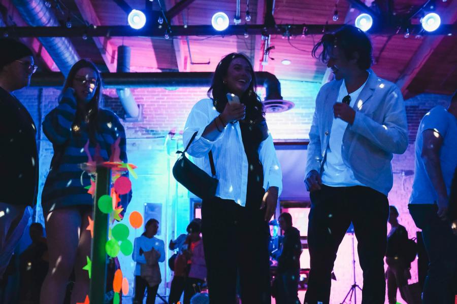 People enjoying a social gathering under colorful lighting in a venue with brick walls and exposed beams.