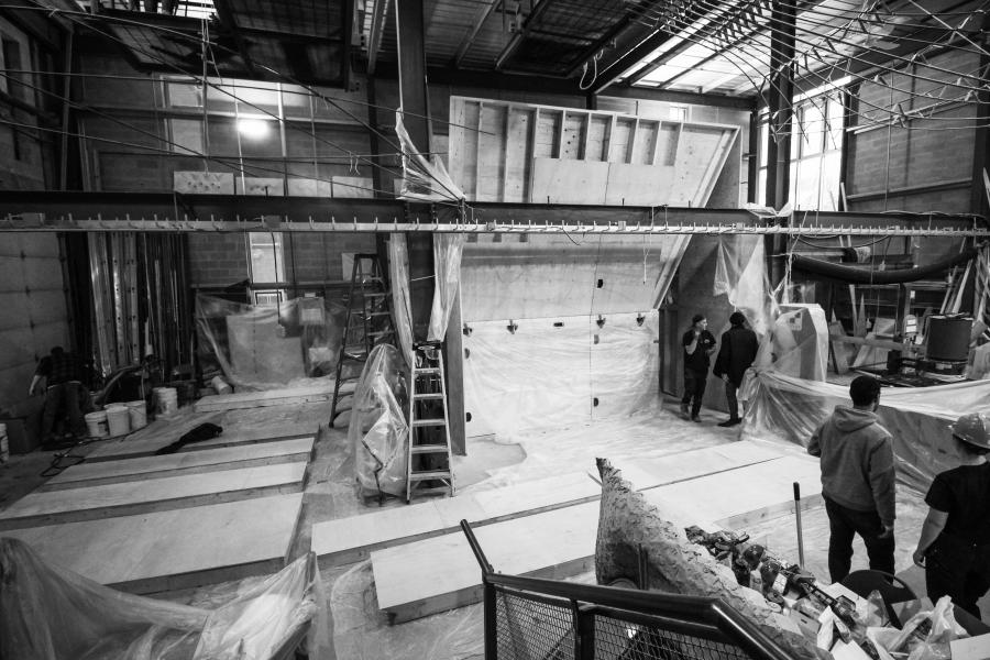 Construction area with workers, wooden panels, and plastic sheets in an industrial setting.