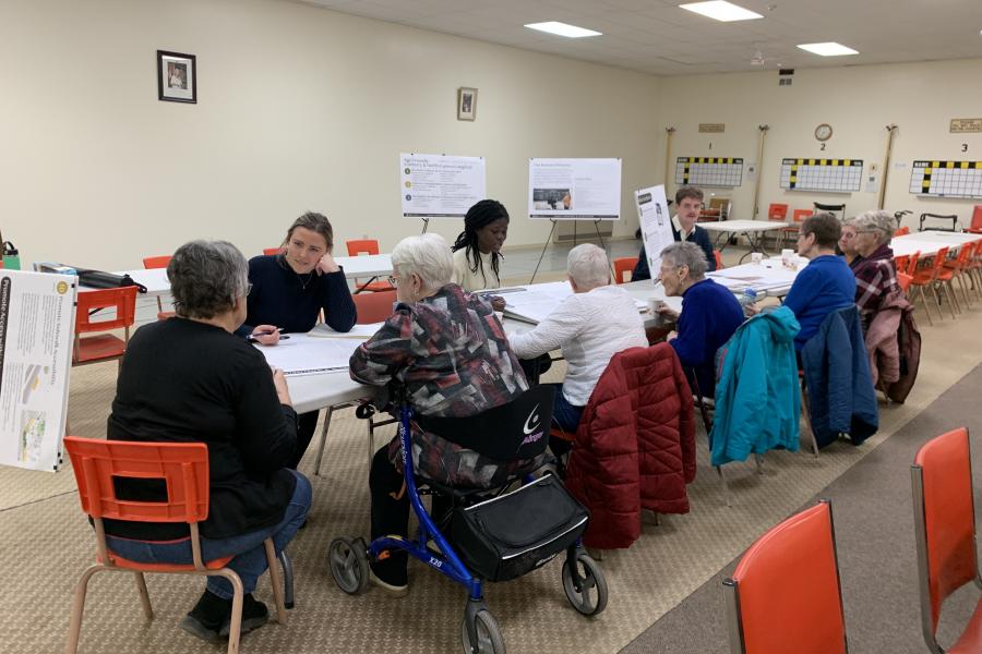 A diverse group of people at tables, examining documents and participating in a group discussion.