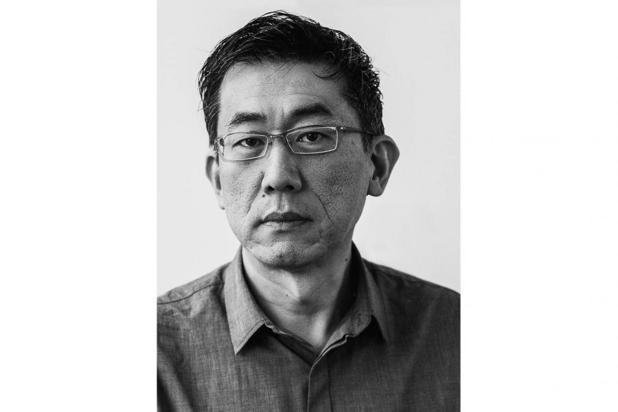 Black and white portrait of an older man wearing glasses and a button-up shirt. He has a serious expression against a plain background.