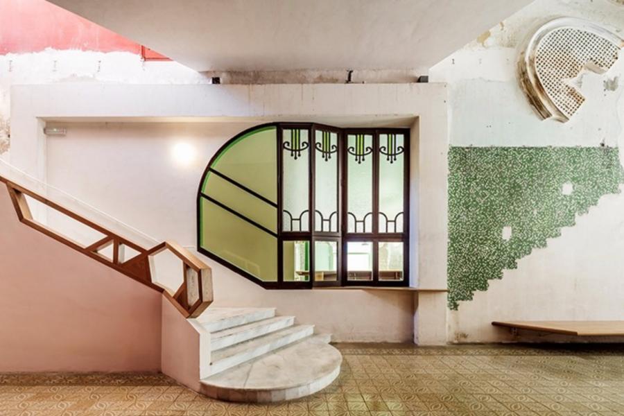 A modern interior features an angular staircase with wood accents against a white wall. Stained glass windows, mosaic tiles, and abstract artwork add style.