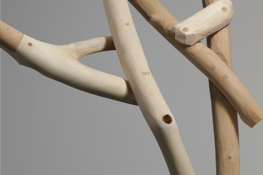 Close-up of intertwined, smooth wooden branches in natural tones on a gray background, showcasing craftsmanship and organic elegance.