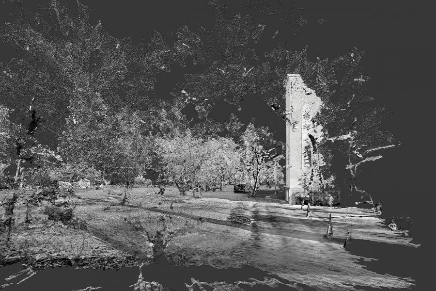 Grayscale image of a park scene. Trees surround a tall, narrow tower at the center. People walk along a path, casting long shadows in the sunlight.