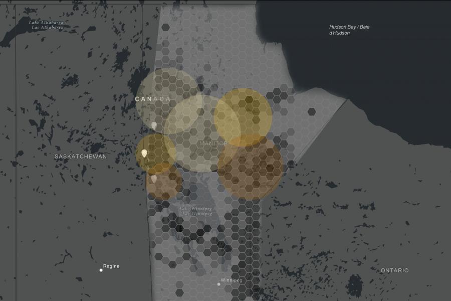 A grayscale map of Manitoba, Canada shows hexagonal grids with overlapping amber and brown circles. Major cities like Winnipeg and Regina are labeled.