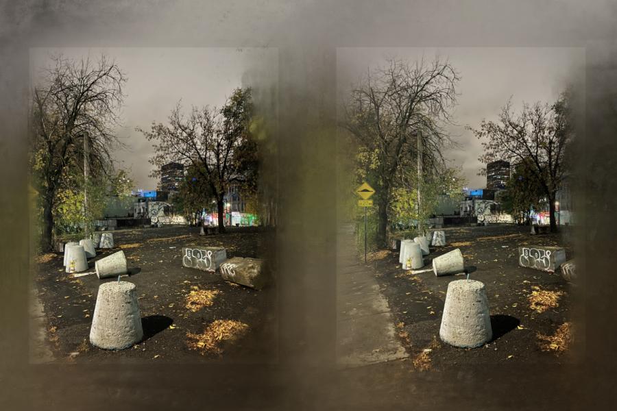 Dimly lit urban scene at night with bare trees, concrete barriers, and graffiti in the foreground. A hazy atmosphere suggests a somber tone.