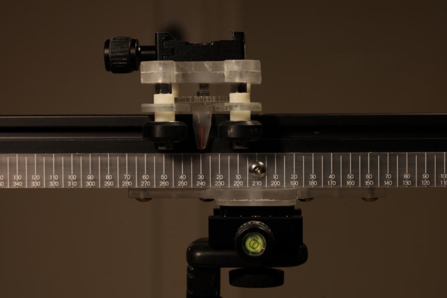 A precise measurement setup with a metallic ruler marked in millimeters, a transparent sliding carriage, and a leveling bubble beneath, suggesting technical focus.