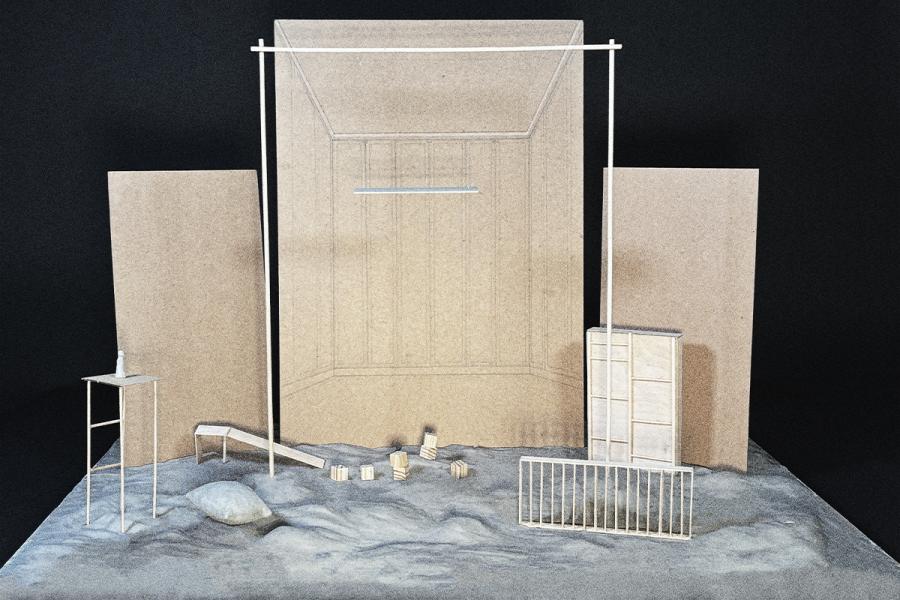 A minimalist architectural model with two tall, rectangular structures and abstract elements on a sandy base, conveying a modern, industrial tone.
