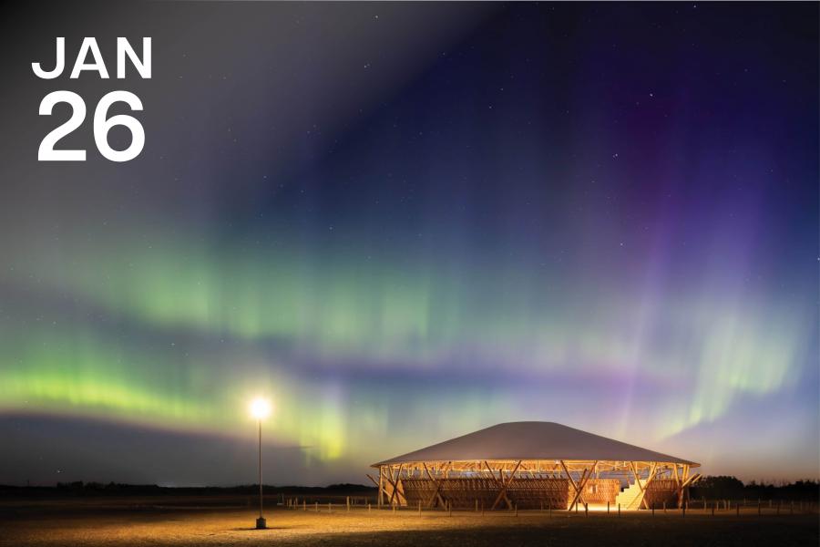 A modern wooden pavilion is illuminated under a vibrant aurora borealis, with green and purple hues filling the night sky. A single streetlamp adds warmth.