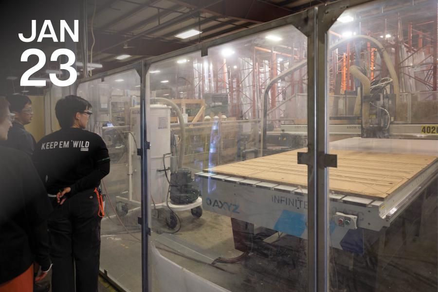 Group of people in safety gear observe a large CNC machine through glass in a factory. The scene conveys a sense of industrial innovation and safety.
