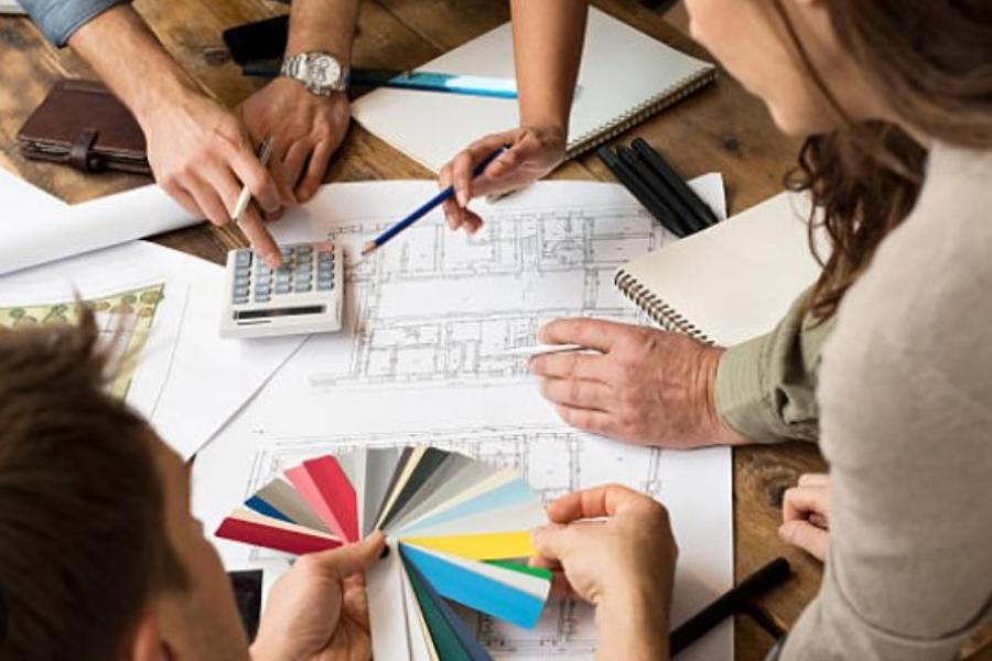 A group discusses architecture plans at a table, with hands pointing at blueprints and holding a color swatch book.