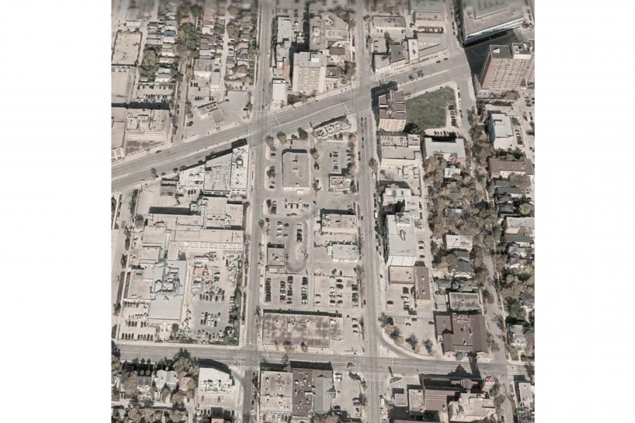 Aerial view of a dense urban neighborhood with intersecting roads, parking lots, commercial buildings, homes, and scattered trees.