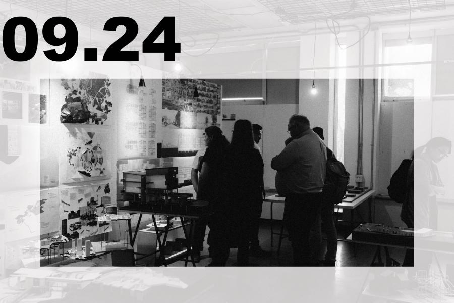 Black-and-white art exhibition in a studio, where visitors view collages and prints amid tables, hanging lights, and industrial fixtures.