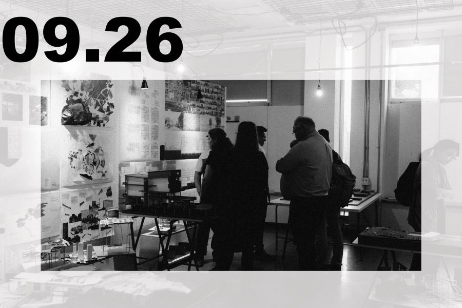 Black-and-white art exhibition in a studio, where visitors view collages and prints amid tables, hanging lights, and industrial fixtures.
