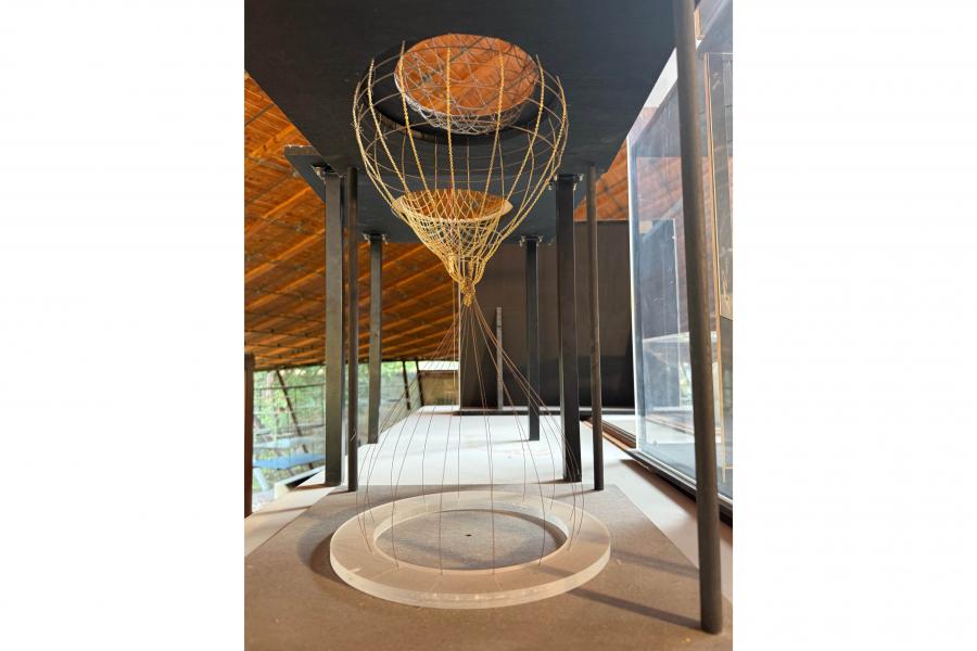 Sculptural wire basketball hoop installation in a sunlit modern gallery, with layered hoops, hanging nets, dark columns, and warm wood ceilings.